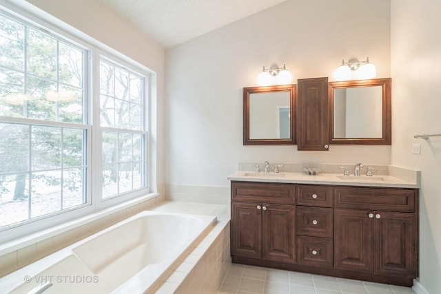 bathroom with a textured ceiling, vanity, tiled bath, and tile patterned floors