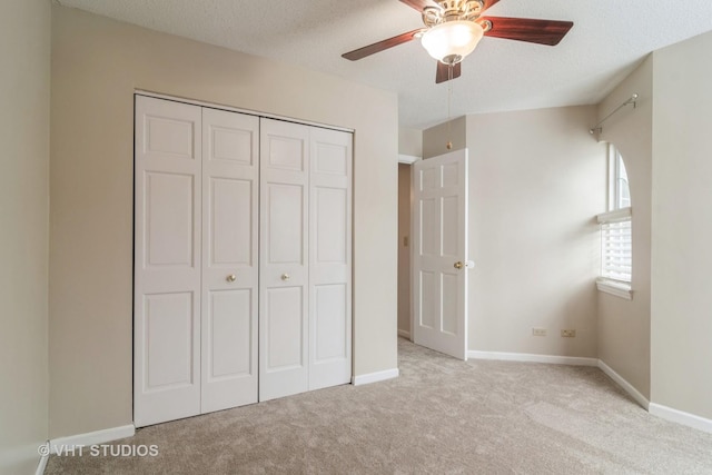 unfurnished bedroom featuring ceiling fan, a closet, light colored carpet, and a textured ceiling