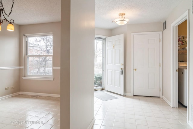 foyer featuring light tile patterned floors, a textured ceiling, washer / clothes dryer, and a notable chandelier