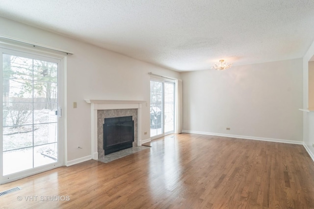 unfurnished living room with a textured ceiling, a fireplace, hardwood / wood-style flooring, and an inviting chandelier