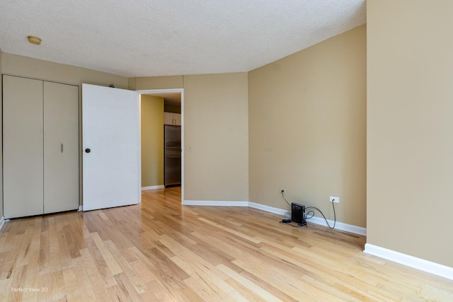 unfurnished bedroom with light wood-type flooring, a textured ceiling, stainless steel refrigerator, and a closet