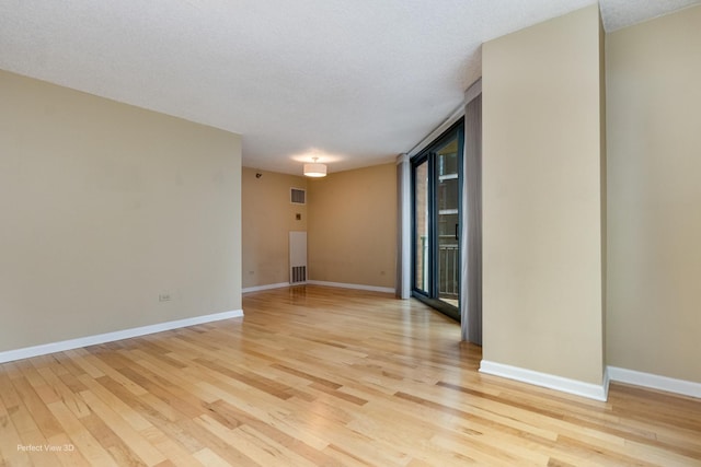 spare room with expansive windows, a textured ceiling, and light hardwood / wood-style flooring