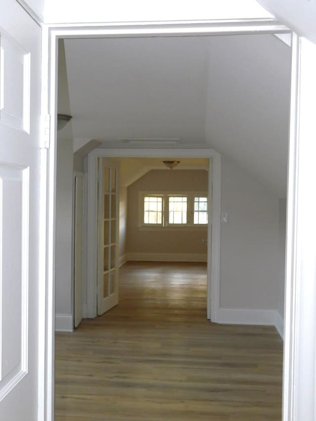 corridor with hardwood / wood-style flooring and vaulted ceiling