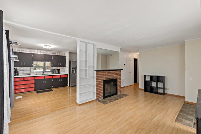 living room featuring sink, light wood-type flooring, and a brick fireplace