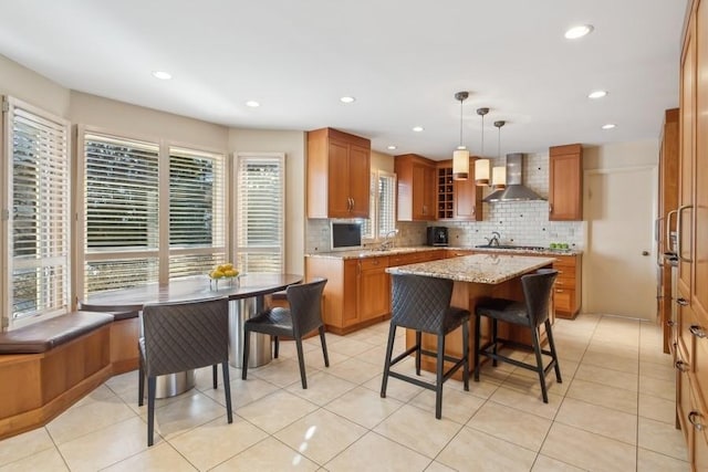 kitchen featuring pendant lighting, a center island, gas stovetop, light stone countertops, and wall chimney exhaust hood