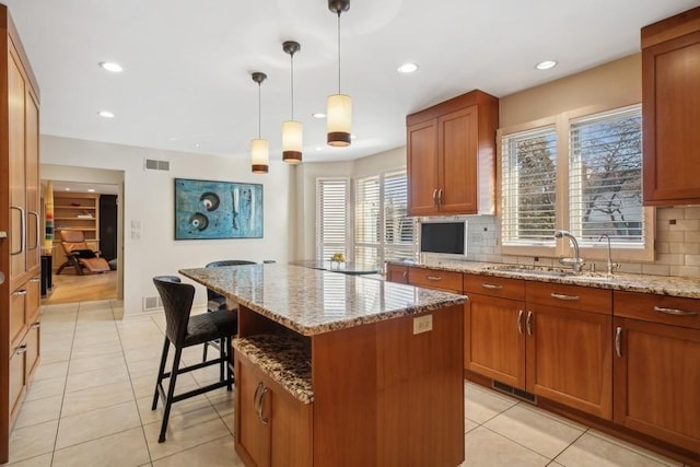 kitchen with a kitchen island, sink, light stone counters, and decorative light fixtures