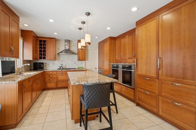 kitchen with a breakfast bar, a center island, pendant lighting, oven, and wall chimney range hood