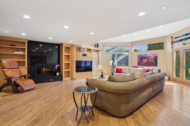 living room with french doors, a large fireplace, built in shelves, and light wood-type flooring