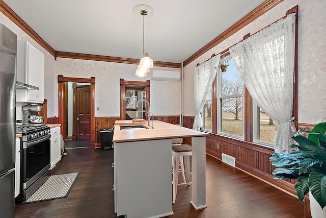 kitchen with a kitchen breakfast bar, a wall mounted AC, a center island with sink, white cabinets, and stainless steel gas stove