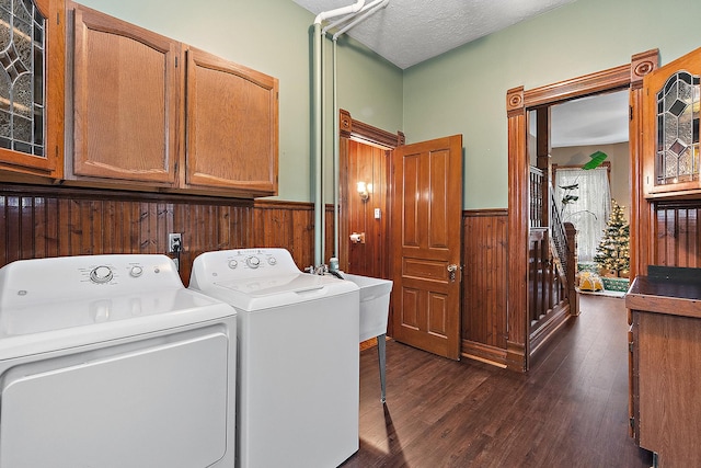 clothes washing area featuring cabinets, dark hardwood / wood-style flooring, a textured ceiling, washing machine and clothes dryer, and wood walls