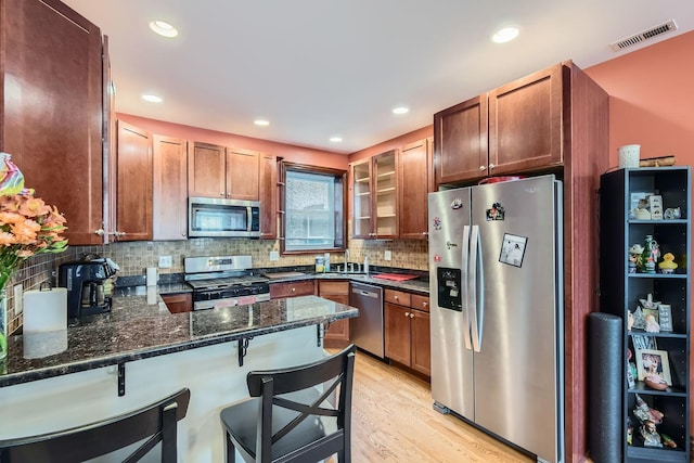 kitchen with kitchen peninsula, stainless steel appliances, dark stone countertops, light hardwood / wood-style floors, and a breakfast bar area