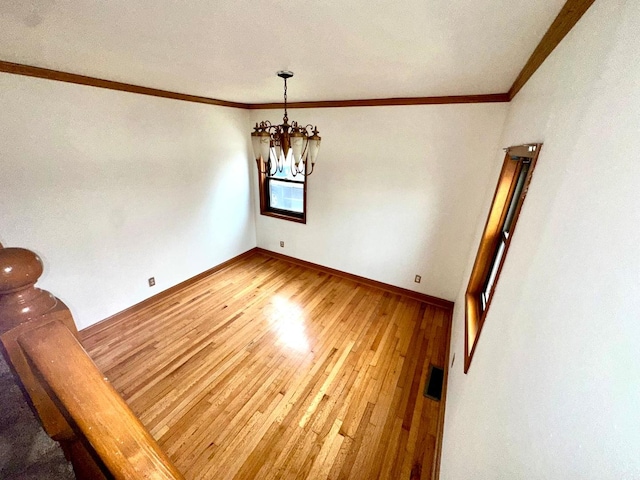 unfurnished dining area featuring wood-type flooring, ornamental molding, and a notable chandelier