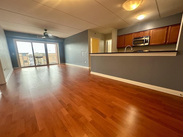 unfurnished living room with wood-type flooring, ceiling fan, and sink