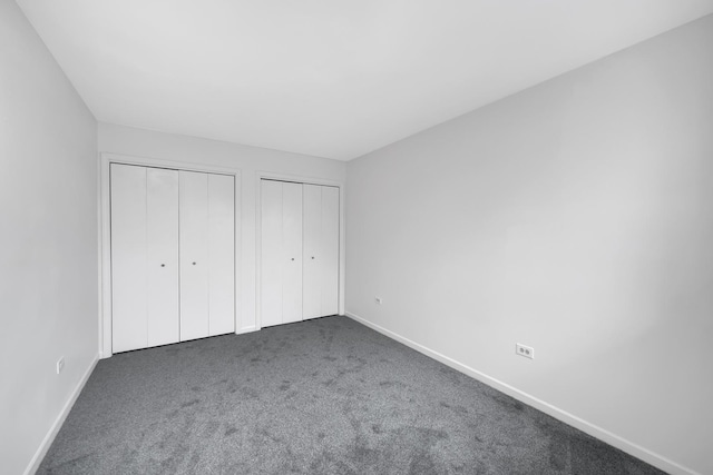 unfurnished bedroom featuring dark colored carpet and multiple closets