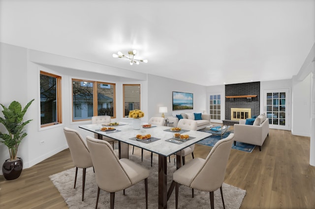 dining area featuring hardwood / wood-style floors, an inviting chandelier, and a brick fireplace