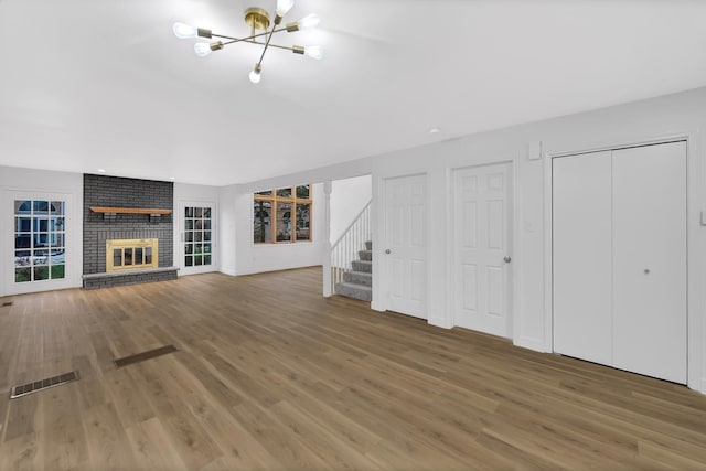 unfurnished living room featuring dark hardwood / wood-style flooring, a chandelier, and a brick fireplace