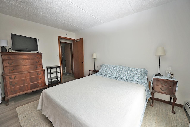 bedroom featuring hardwood / wood-style floors, a textured ceiling, and a baseboard heating unit