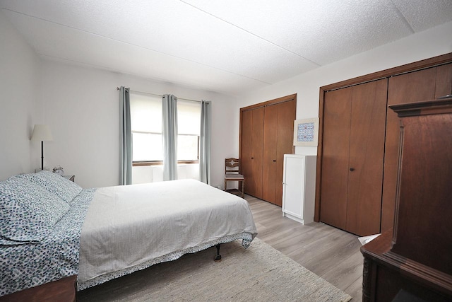 bedroom featuring two closets, a textured ceiling, and light hardwood / wood-style floors