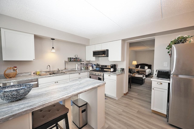 kitchen with sink, light hardwood / wood-style flooring, hanging light fixtures, stainless steel appliances, and white cabinets