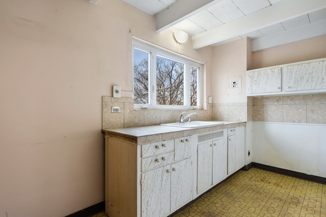 kitchen featuring beam ceiling, backsplash, sink, and white cabinets