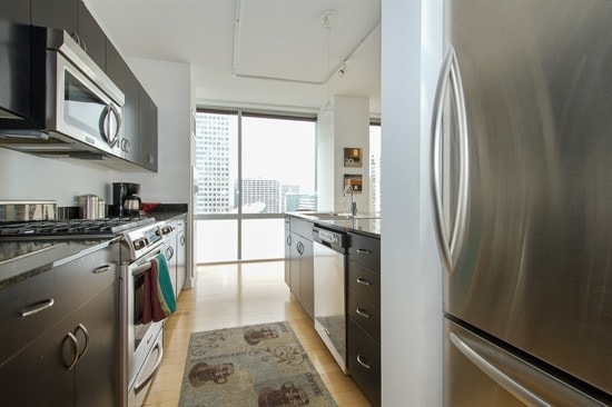 kitchen featuring floor to ceiling windows, track lighting, sink, light wood-type flooring, and appliances with stainless steel finishes