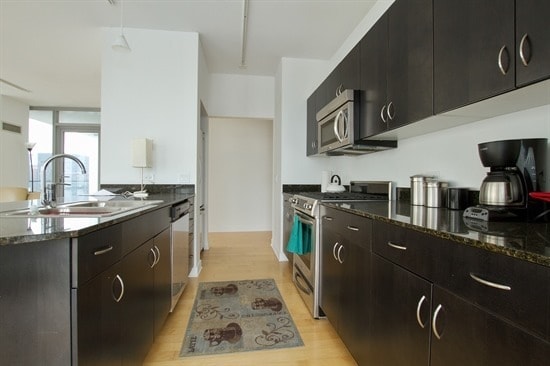 kitchen with dark stone countertops, sink, stainless steel appliances, and light wood-type flooring