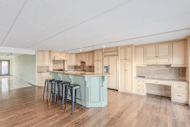 kitchen with sink, paneled built in fridge, light hardwood / wood-style floors, a breakfast bar area, and a kitchen island with sink