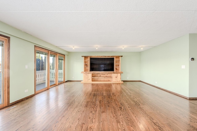 unfurnished living room with a textured ceiling, light hardwood / wood-style floors, and rail lighting