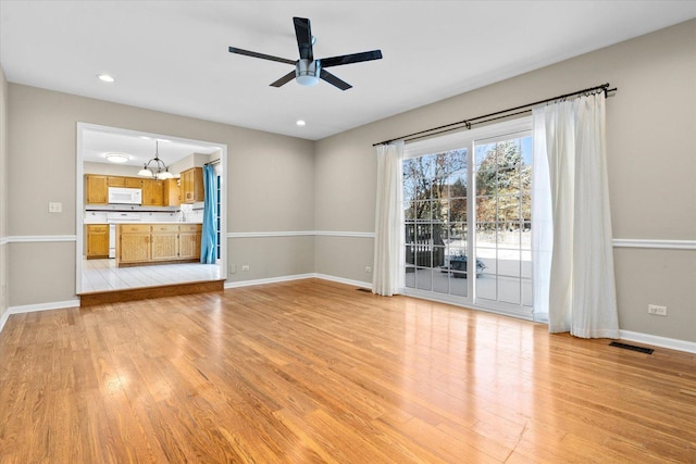 unfurnished living room with ceiling fan with notable chandelier and light hardwood / wood-style floors