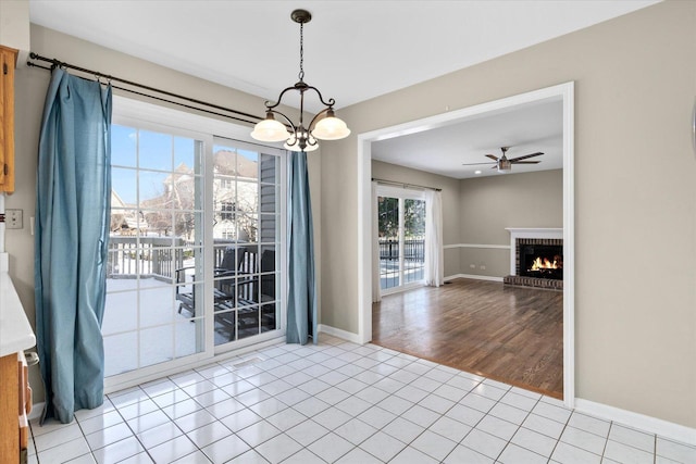 unfurnished dining area featuring a fireplace, ceiling fan with notable chandelier, and light tile patterned flooring