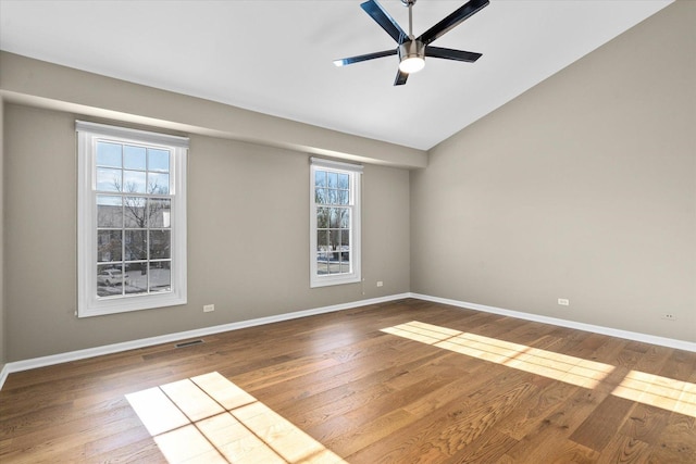 empty room featuring hardwood / wood-style floors, vaulted ceiling, ceiling fan, and a healthy amount of sunlight