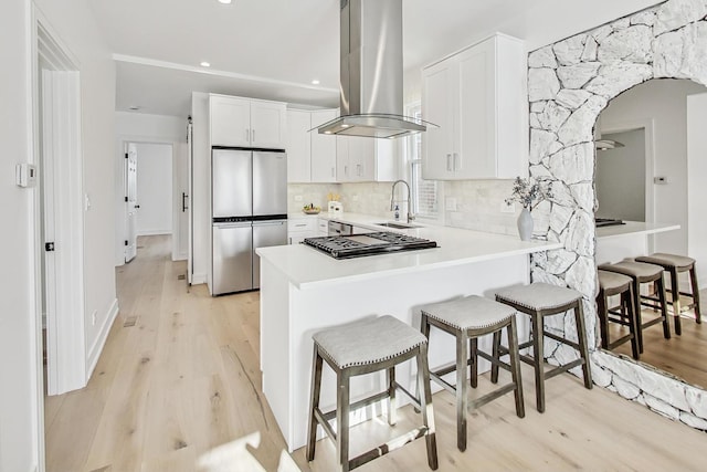 kitchen featuring appliances with stainless steel finishes, white cabinetry, sink, decorative backsplash, and island exhaust hood