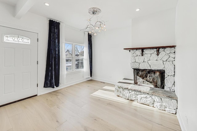 entrance foyer with beam ceiling, an inviting chandelier, a fireplace, and light hardwood / wood-style flooring