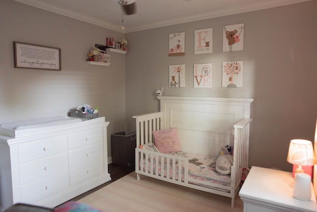 bedroom with ceiling fan, light hardwood / wood-style flooring, a crib, and ornamental molding