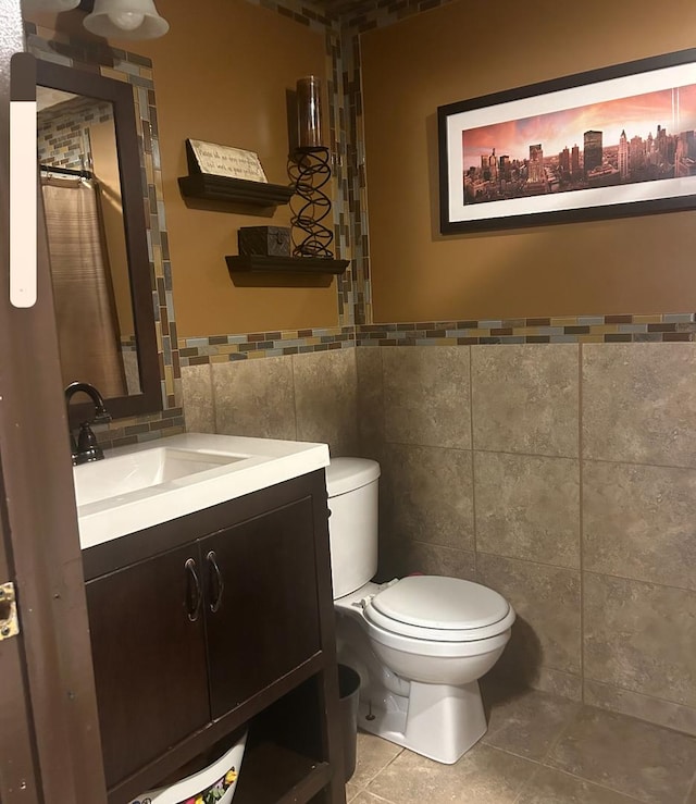 bathroom with tile patterned flooring, vanity, toilet, and tile walls