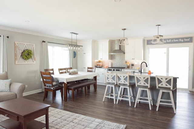 kitchen with a kitchen bar, wall chimney exhaust hood, a kitchen island with sink, decorative light fixtures, and white cabinets