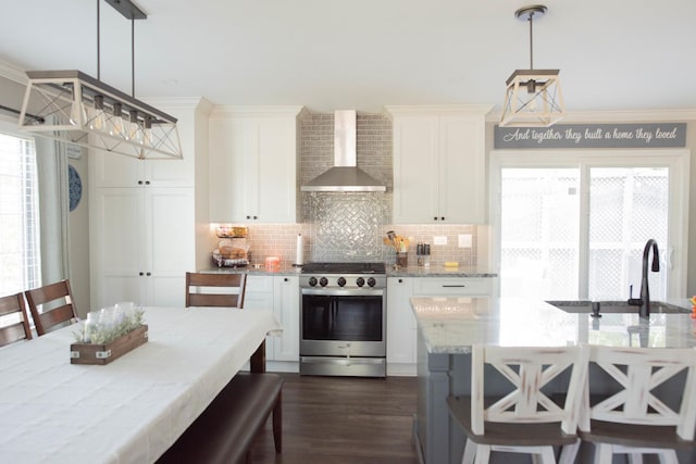 kitchen with stainless steel range with gas stovetop, decorative light fixtures, light stone counters, and wall chimney range hood