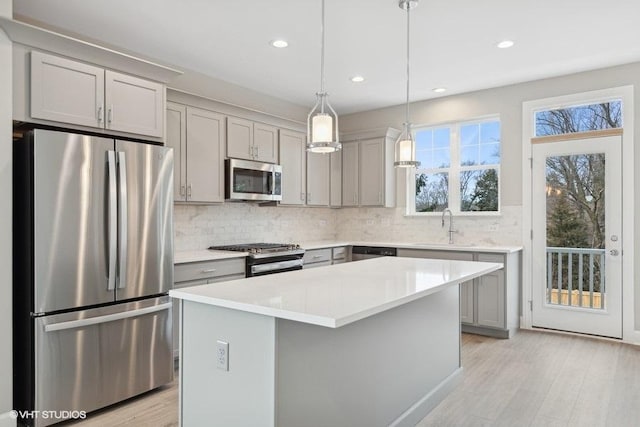 kitchen with sink, a center island, stainless steel appliances, decorative light fixtures, and gray cabinets