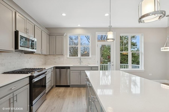 kitchen with sink, stainless steel appliances, pendant lighting, gray cabinets, and decorative backsplash