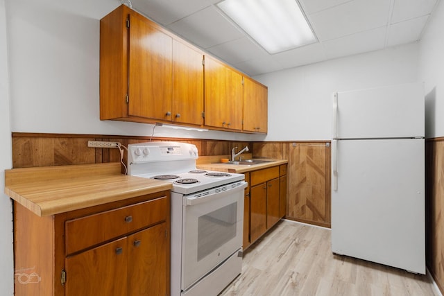 kitchen featuring white appliances, wooden walls, sink, and light hardwood / wood-style flooring