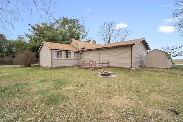 rear view of property featuring a wooden deck, a fire pit, a lawn, and a storage shed