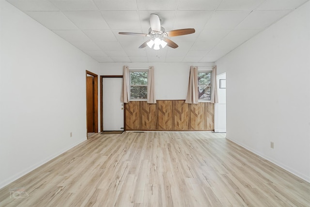 unfurnished room featuring light hardwood / wood-style floors, ceiling fan, and wood walls