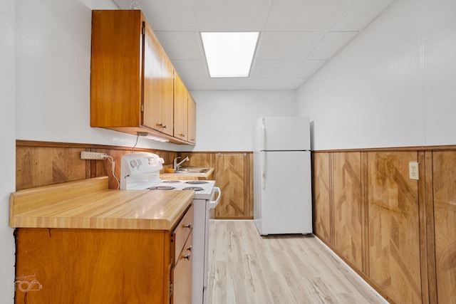 kitchen with sink, light hardwood / wood-style flooring, wooden walls, white appliances, and a drop ceiling