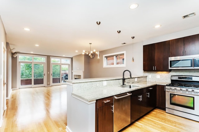 kitchen with sink, tasteful backsplash, light stone counters, appliances with stainless steel finishes, and kitchen peninsula