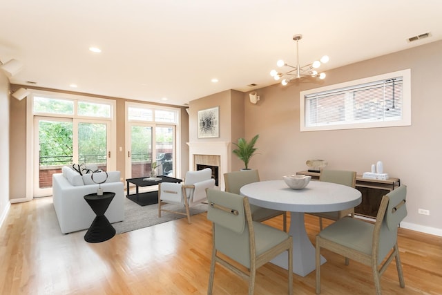 dining space featuring a notable chandelier, a fireplace, and light wood-type flooring