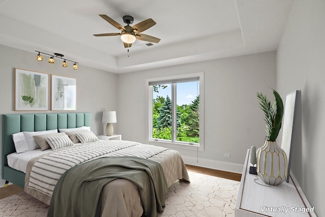 bedroom featuring light hardwood / wood-style floors, a raised ceiling, and ceiling fan