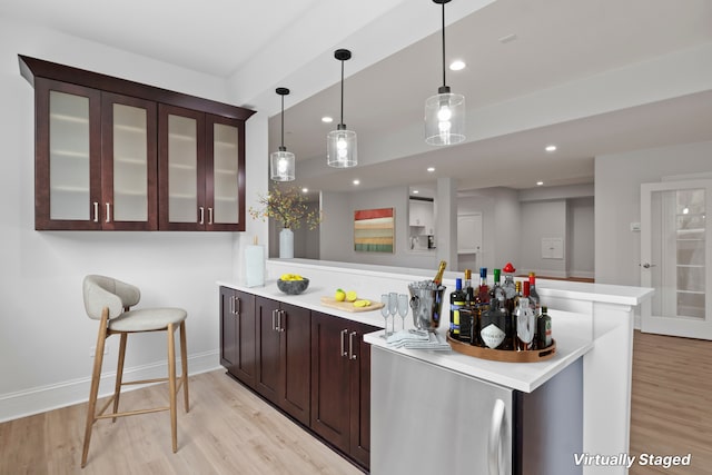 bar featuring dark brown cabinetry, decorative light fixtures, and light hardwood / wood-style flooring