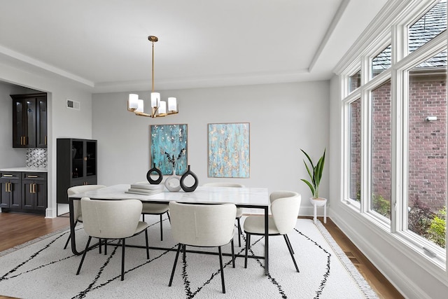 dining space featuring hardwood / wood-style flooring, a raised ceiling, and a notable chandelier