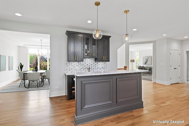 kitchen featuring a kitchen island, decorative light fixtures, beverage cooler, decorative backsplash, and light hardwood / wood-style flooring