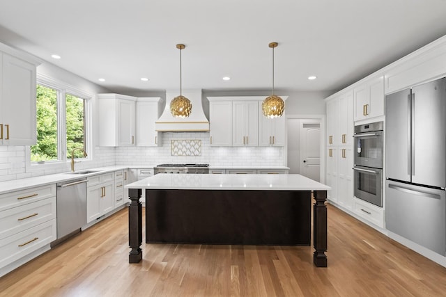 kitchen with white cabinetry, decorative light fixtures, appliances with stainless steel finishes, custom range hood, and a kitchen island